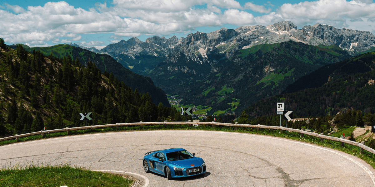 An Audi R8 rounds a hairpin with the Austrian alps in the background